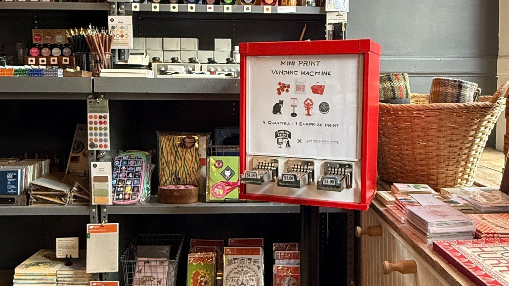 A red vending machine with a sign that shows the art prints it dispenses. It sits in a shop near shelves filled with stationery supplies.