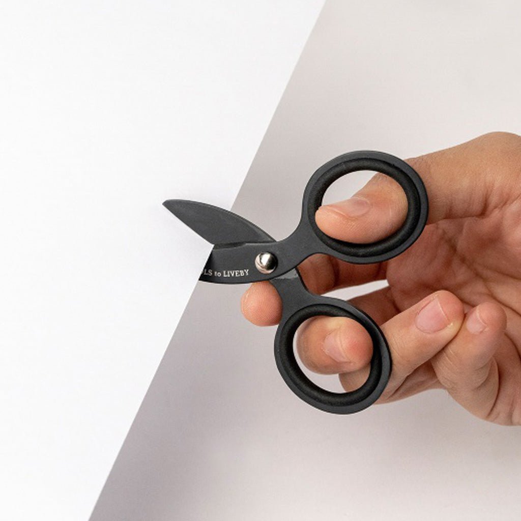 Hand using small black scissors to cut sheet of white paper
