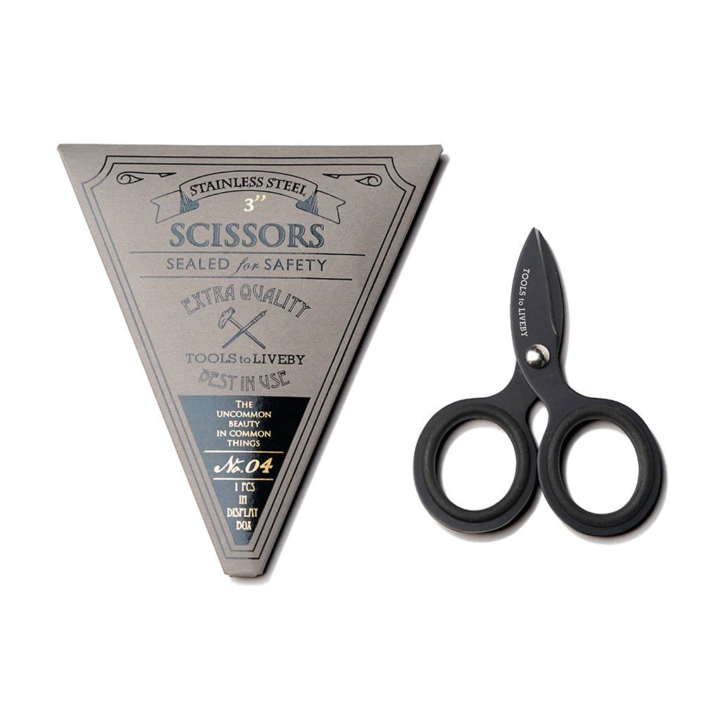 Pair of small three inch black steel scissors next to gray triangular packaging with Tools to Liveby branding on white background