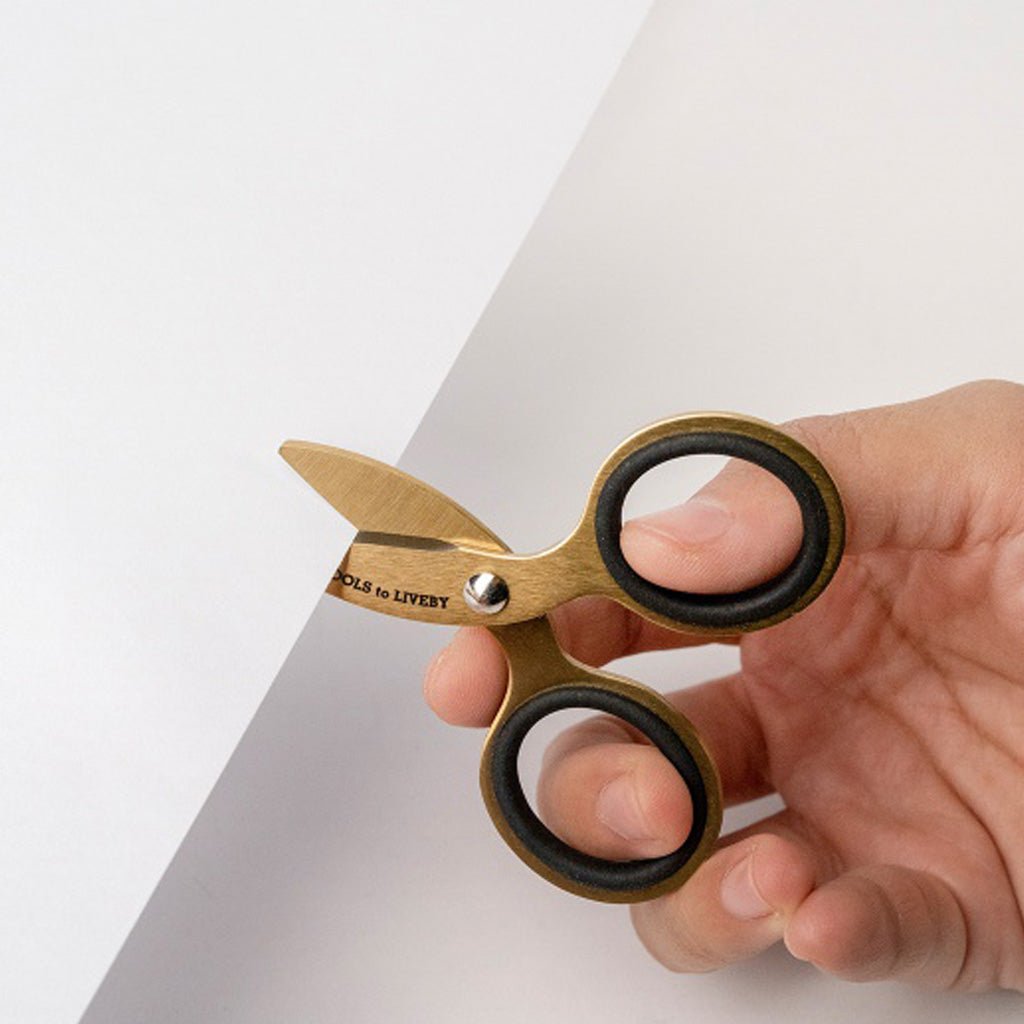Hand using small gold scissors to cut sheet of white paper