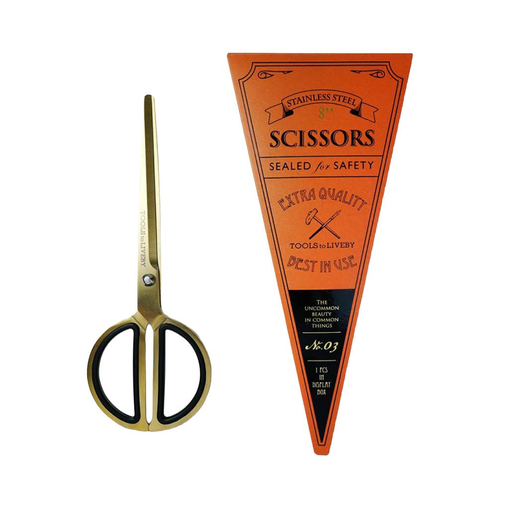 Vintage-style pocket scissors with gold-toned blades and black handles, shown next to an orange triangular paper label that reads 'Scissors' and 'Sealed for Safety' on a plain white background.