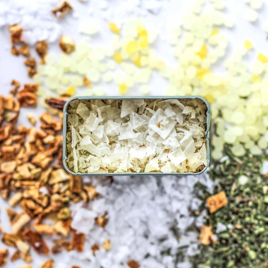 Open tin of aegean salt blend surrounded by spices on white background
