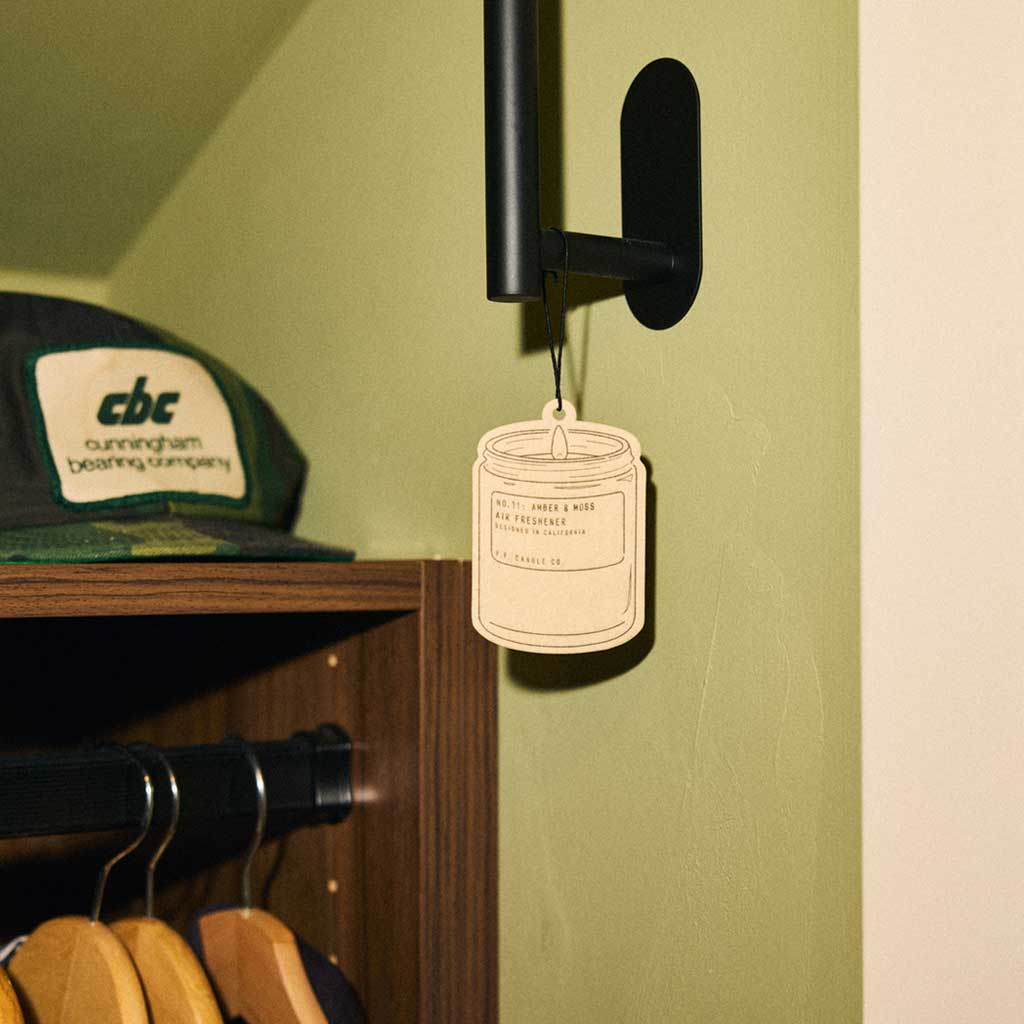 Air freshener hanging on a hook with a green wall and wooden shelf in the background.