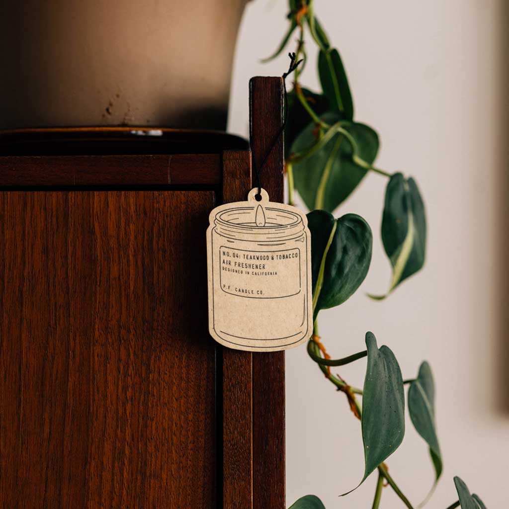Air freshener tag hanging from a wooden cabinet with a plant in the background