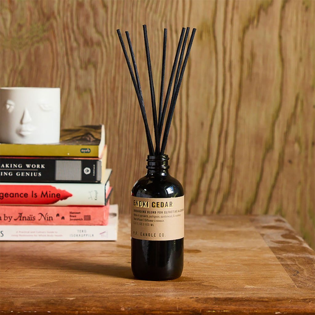 Enoki cedar diffuser bottle with sticks on a wooden surface with books in the background