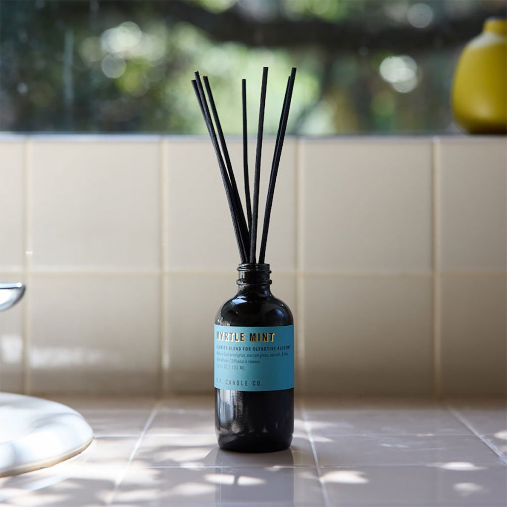 Myrtle mint reed diffuser bottle with black sticks on a tiled surface