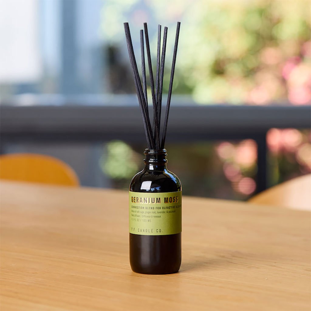 Geranium moss diffuser bottle with reeds on a wooden surface, blurred outdoor background