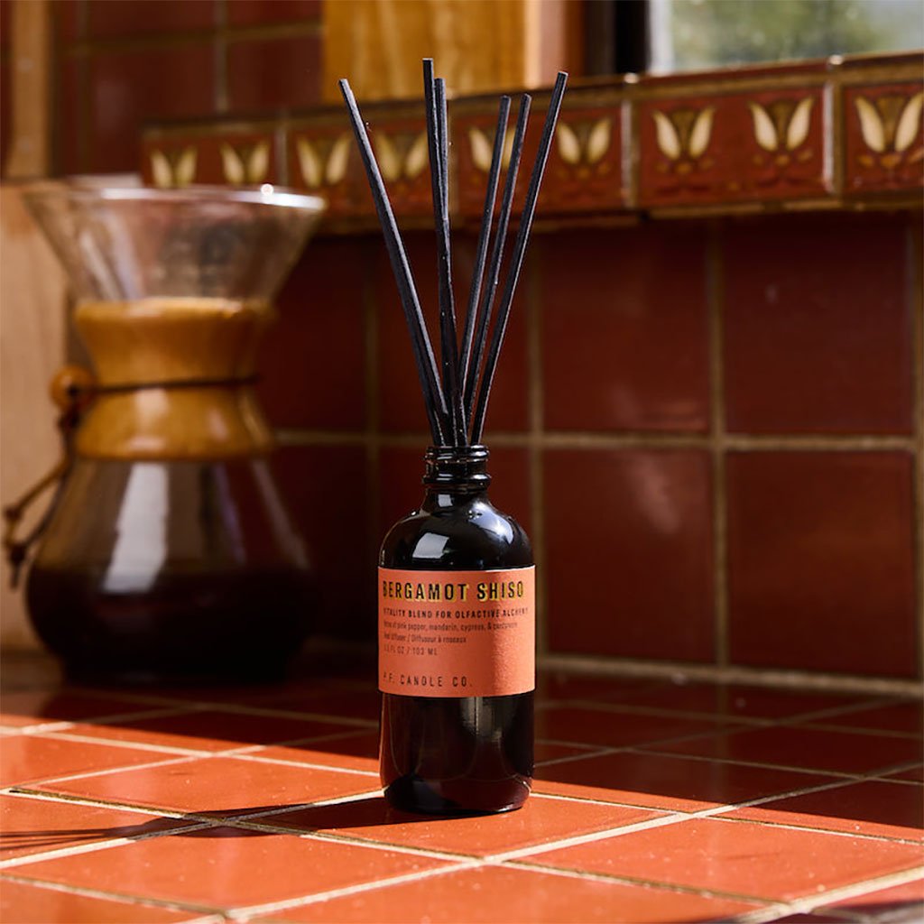 Bottle of bergamot shiso diffuser with a red label on a red tiled surface