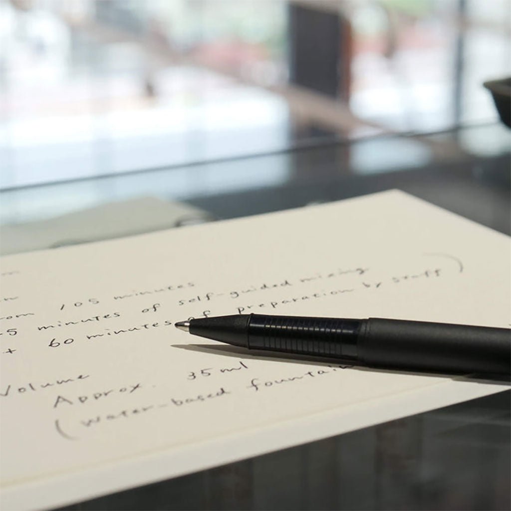 Black pen on a piece of paper with handwritten text, blurred background