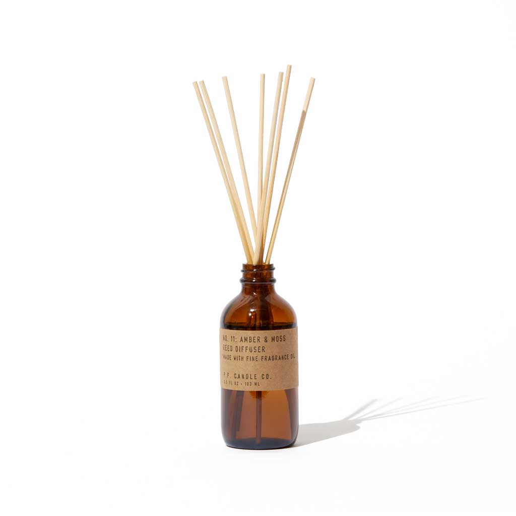 Reed diffuser with wooden sticks in an amber glass bottle on a white background