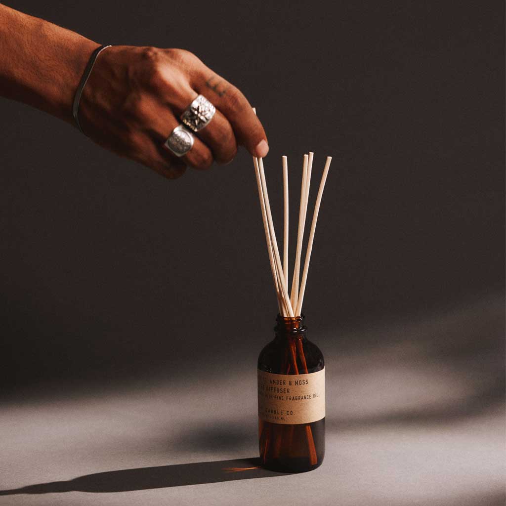 Hand placing reed diffuser sticks into a bottle with a label on a dark background