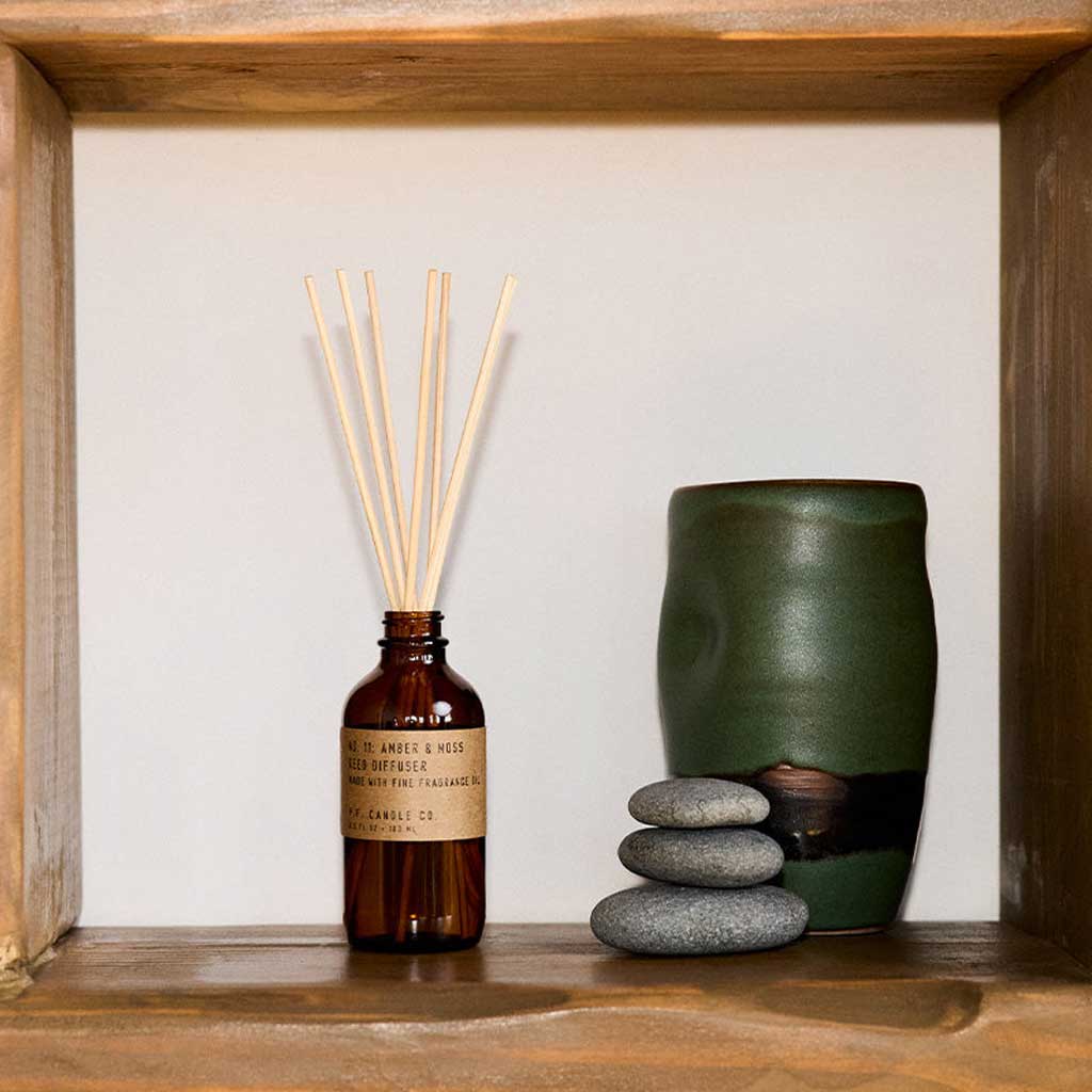Aromatherapy diffuser with reeds and a green ceramic vase on a wooden shelf.