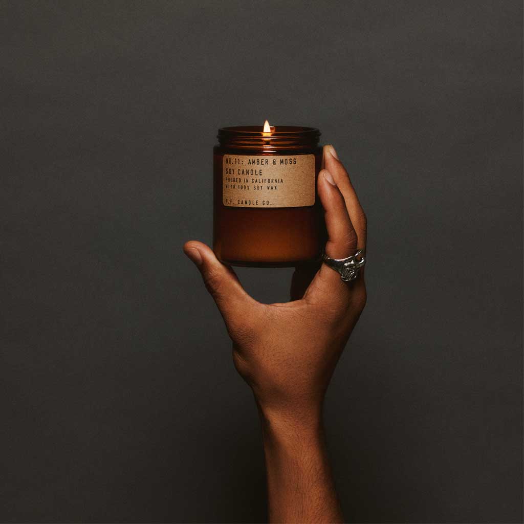 Hand holding a lit candle with a label against a dark background