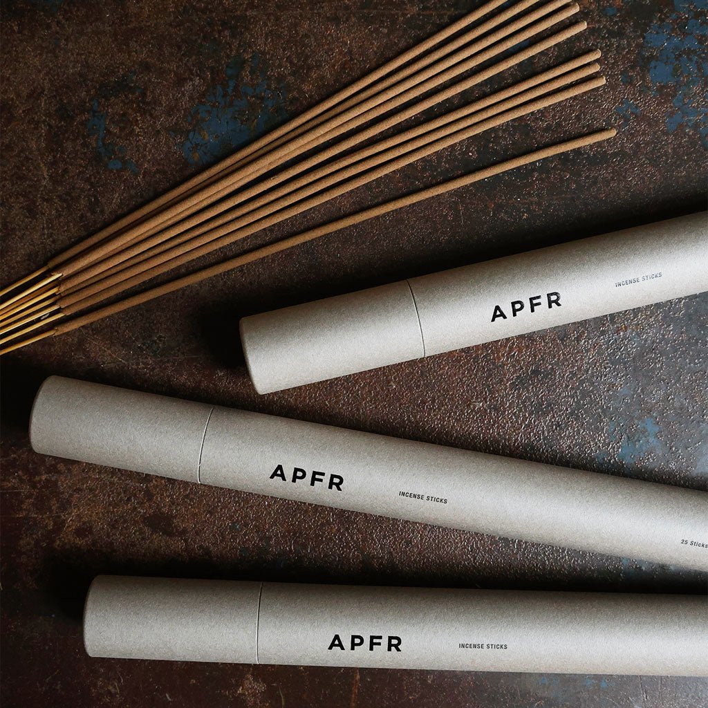 Tubes of APFR incense next to incense sticks on dark background