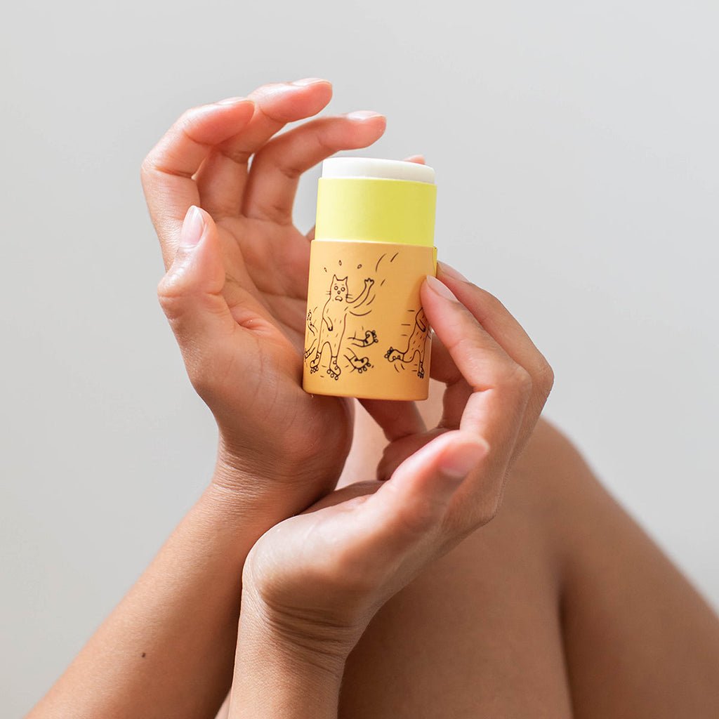 Hand holding a yellow and white container with a design on a light gray background