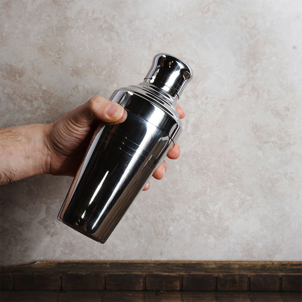 Hand holding a shiny metal cocktail shaker against a neutral background