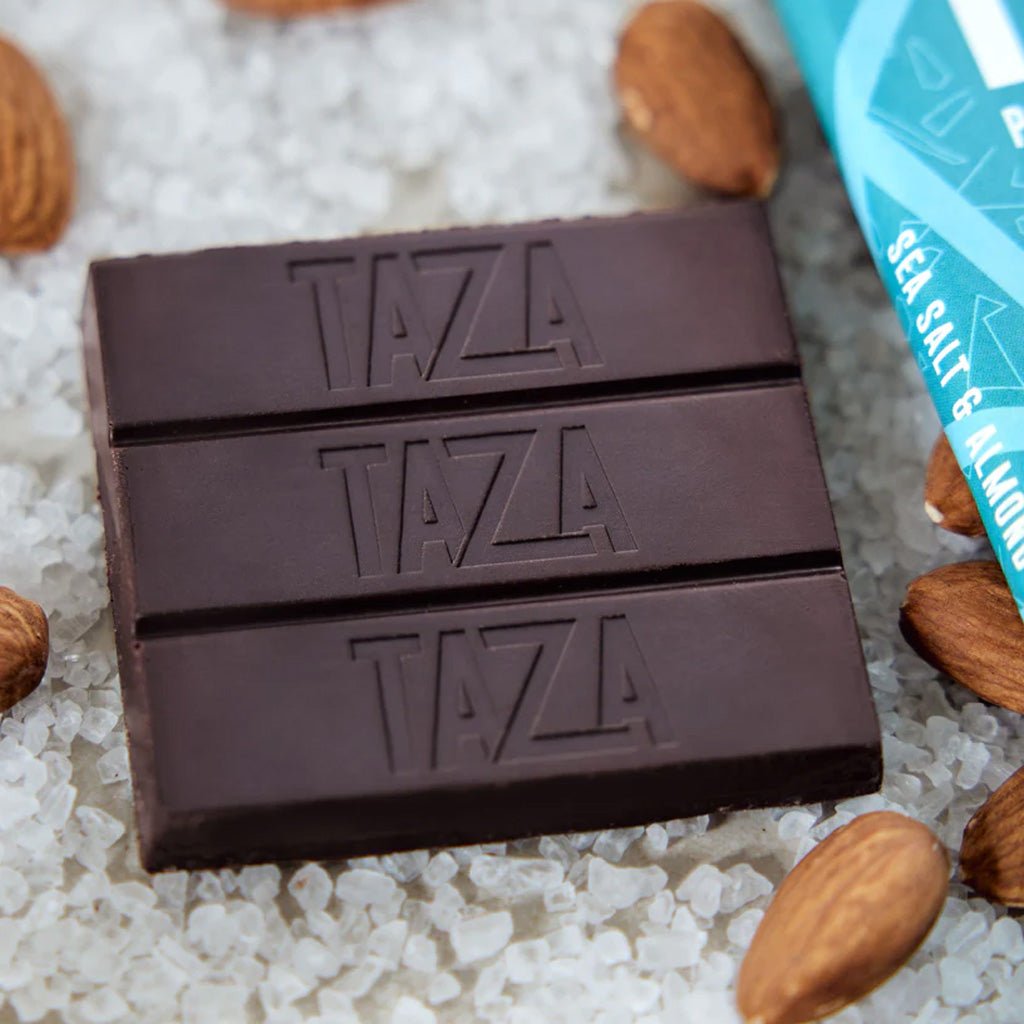 Two Taza chocolate bars on pile of sea salt with almonds around