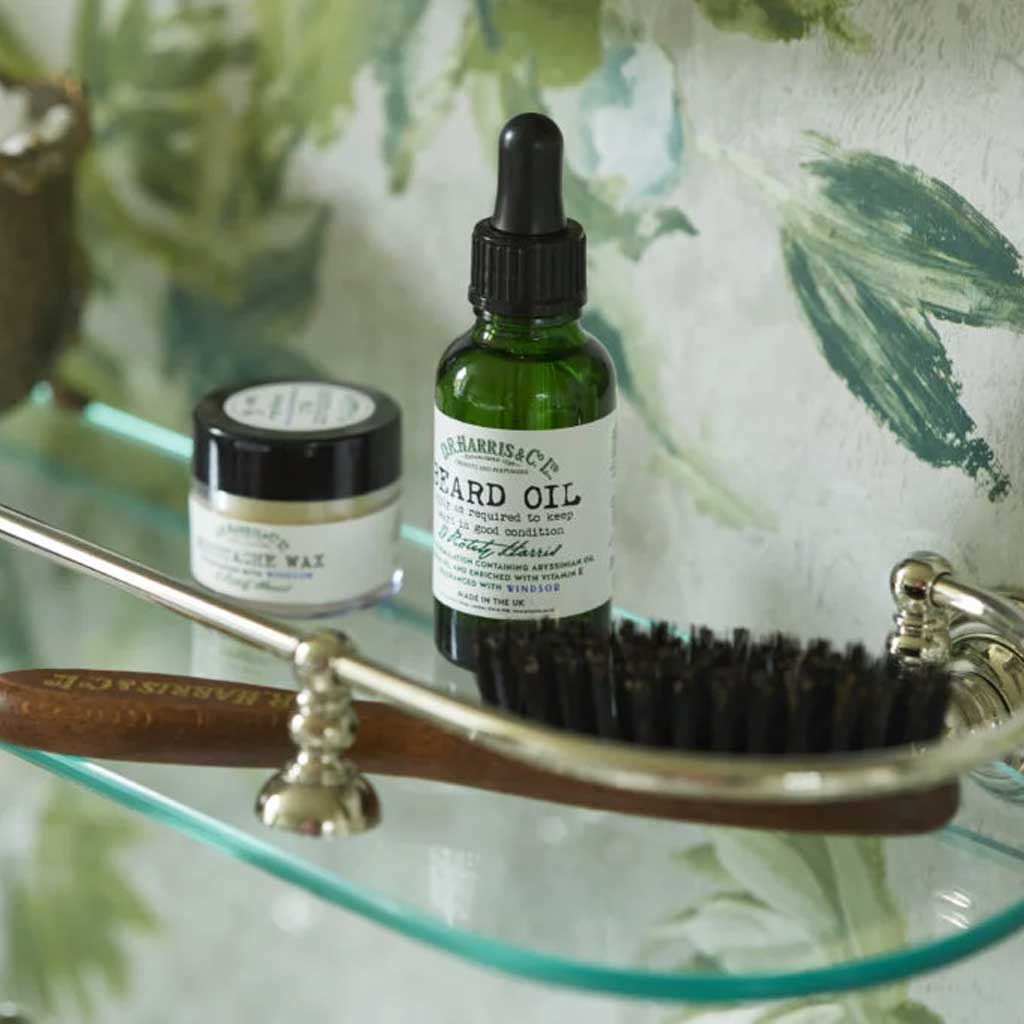 Bottle of beard oil with a brush and jar on a glass tray with a floral background