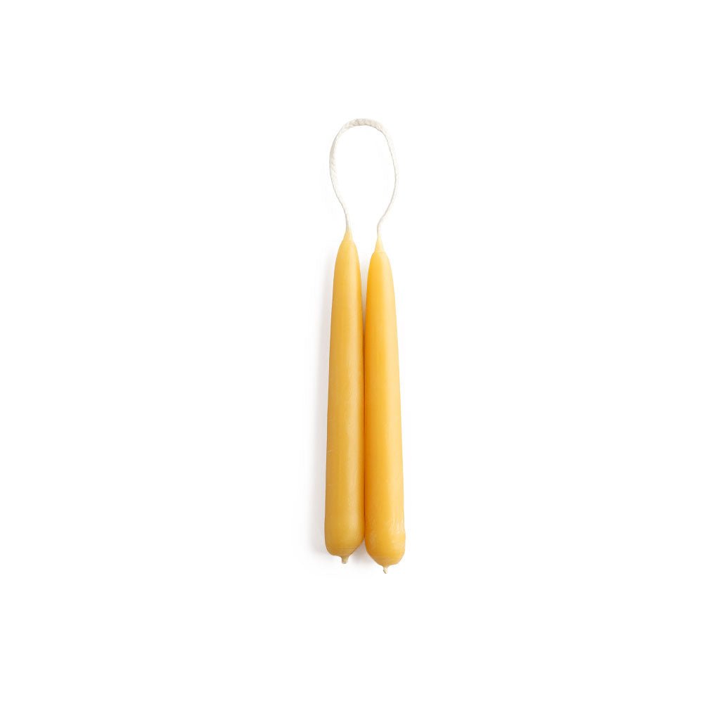 A set of two thin, short yellow beeswax taper candles on white background