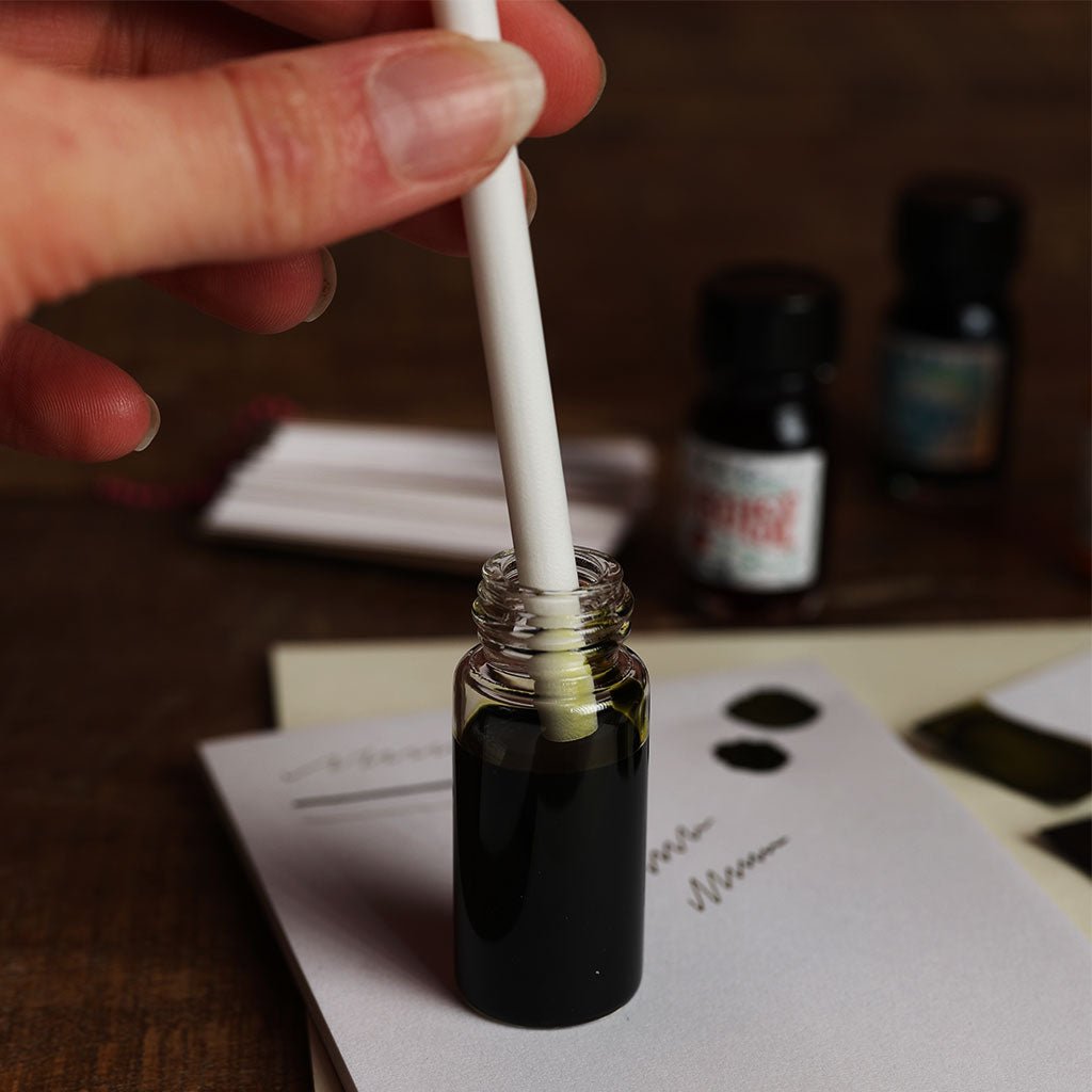 Hand holding a dropper over a small bottle of dark liquid with a blurred background