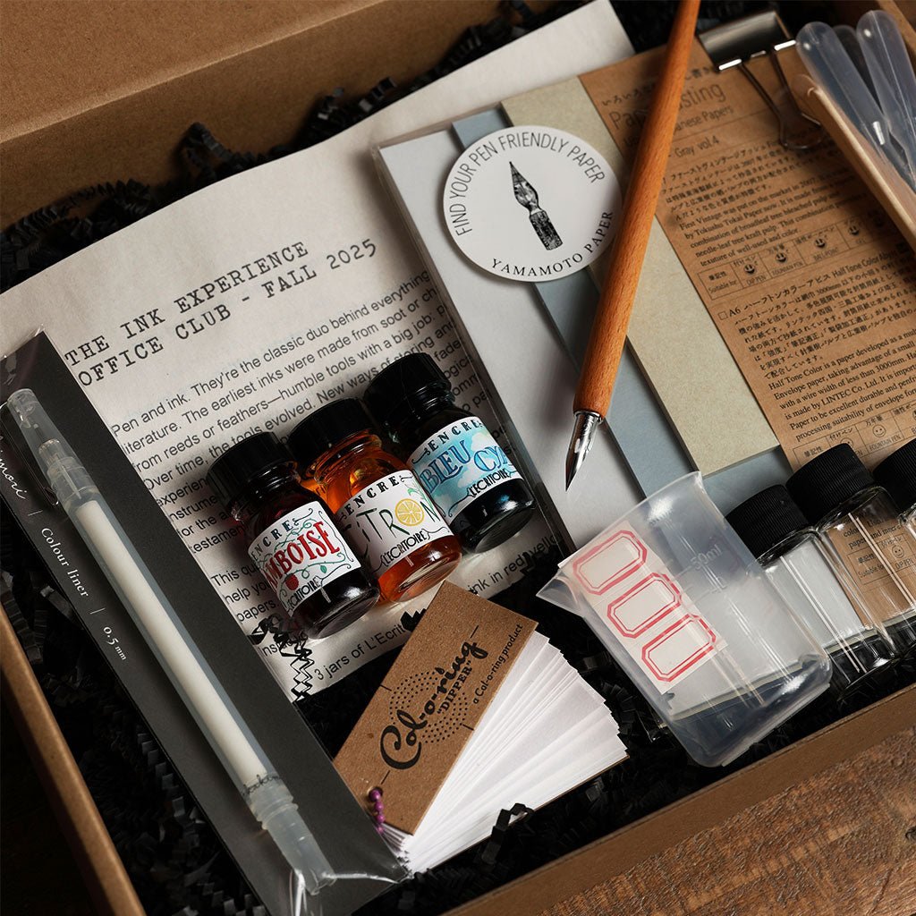 Collection of ink bottles, a pen, and stationery items in an open box with text and branding visible.