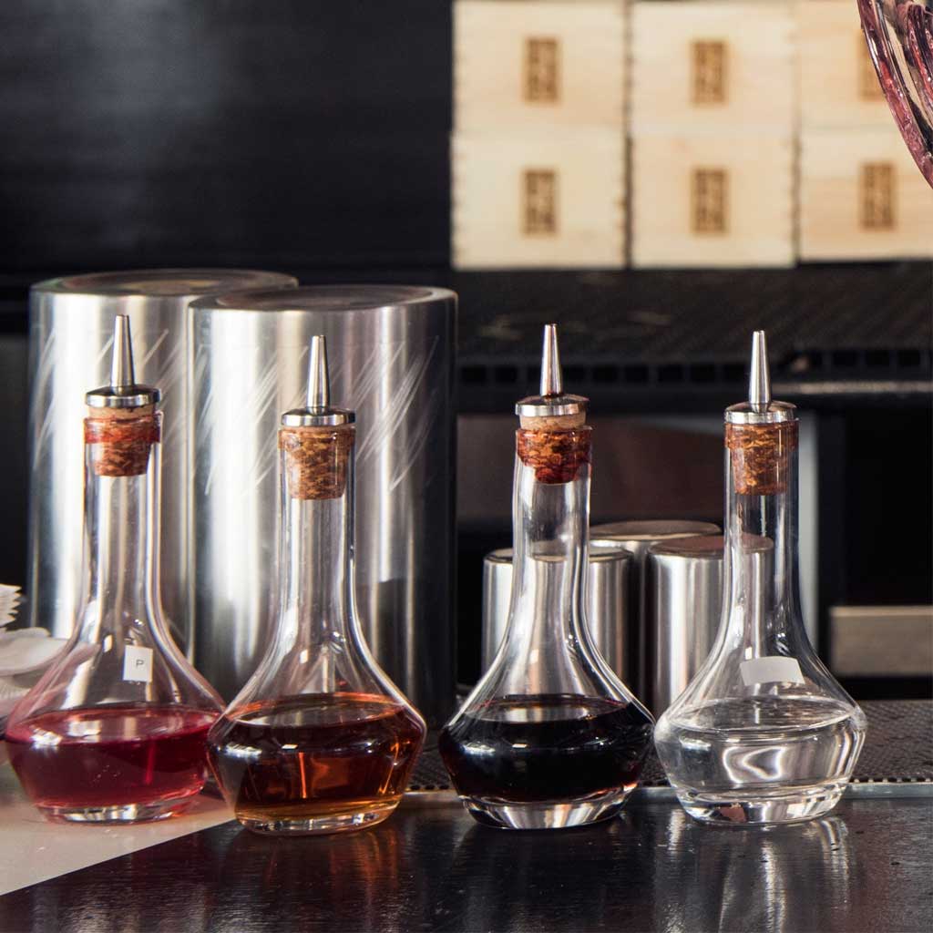 Four glass bitter bottles with cork and stainless steel dashers on a bar top.