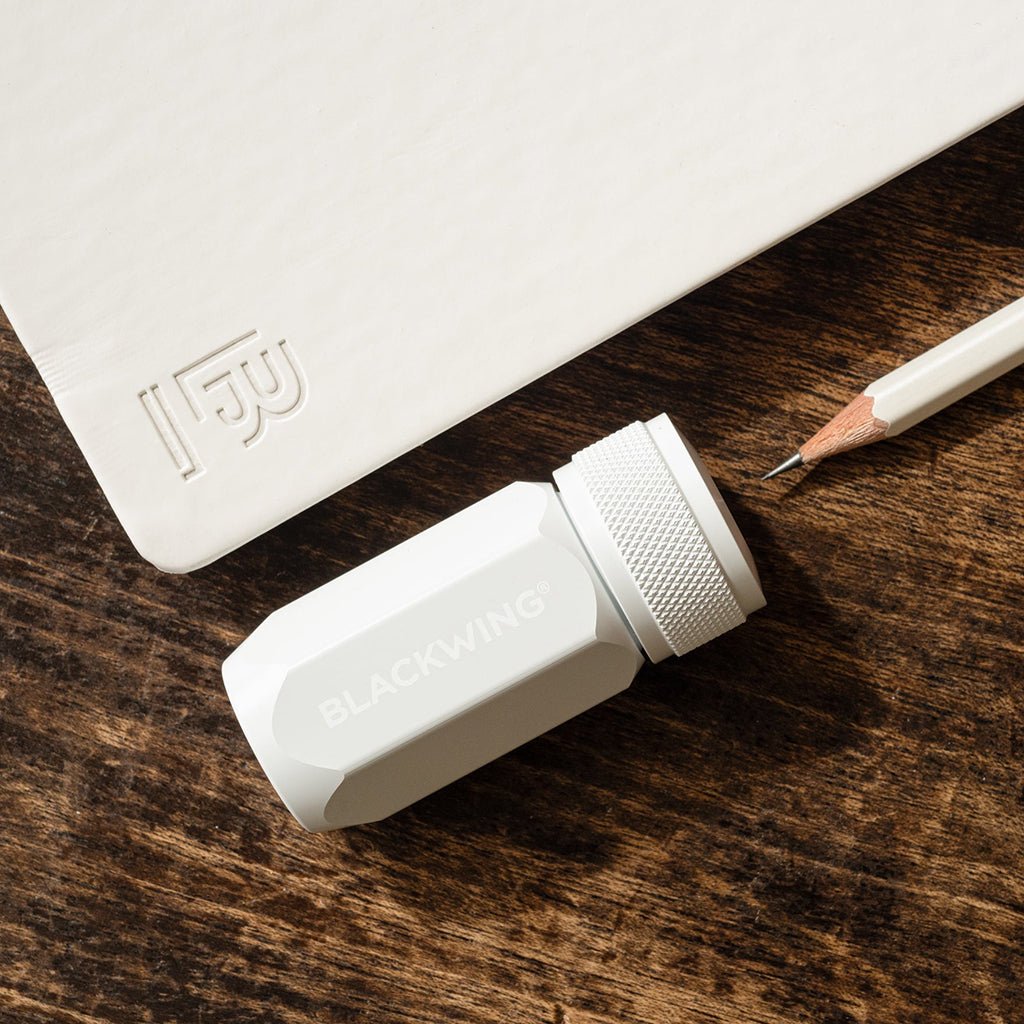 White Blackwing sharpener with pencil and notebook on wooden surface