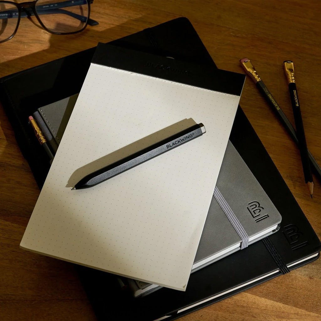 Stack of Blackwing stationery on wooden desk with Blackwing pen on top