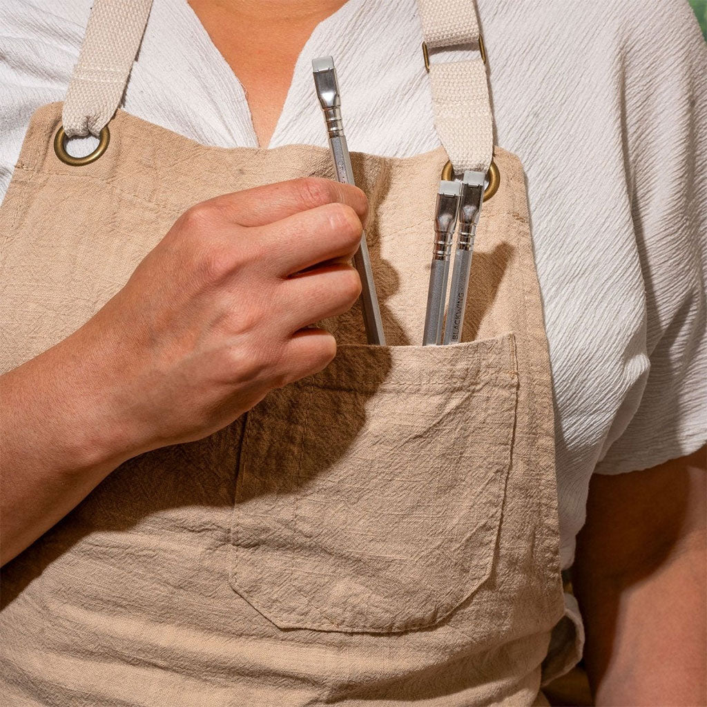 Three Blackwing Volumes 140 pencils are tucked into the pocket of an apron worn by a person wearing a white shirt.
