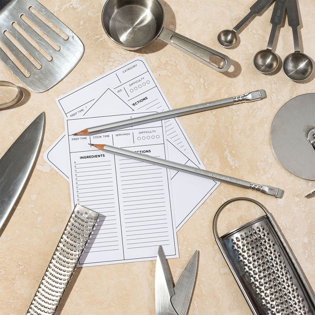 Two Blackwing Volumes 140 pencils sit on a countertop with recipe cards and stainless steel kitchen tools.