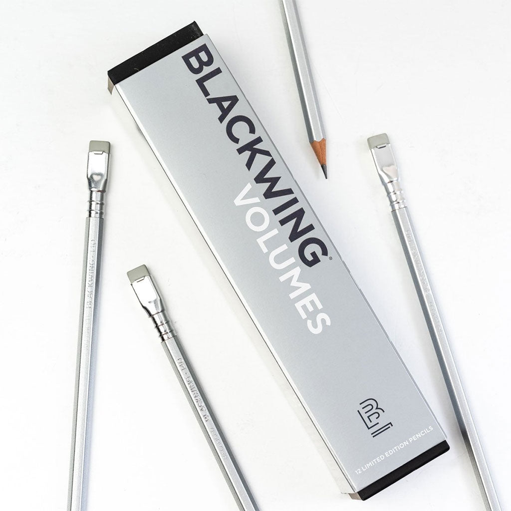 A box of Blackwing Volumes 140 pencils on a white background. Four pencils are scattered around the box.