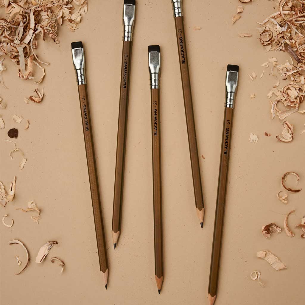 Five Blackwing Volumes 21 pencils on a tan surface, surrounded by wood shavings.