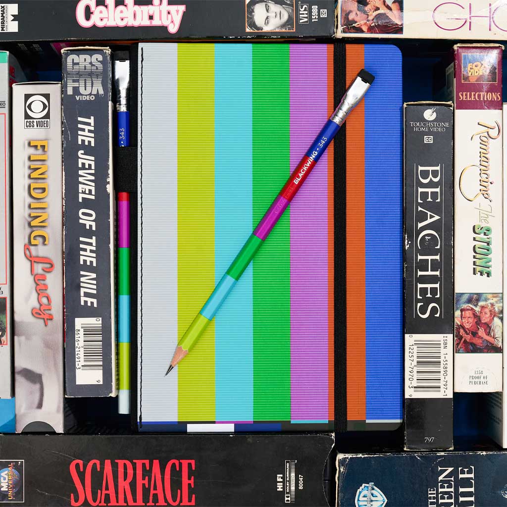 Blackwing 343 notebook with color bar cover and pencil surrounded by vintage VHS tapes.