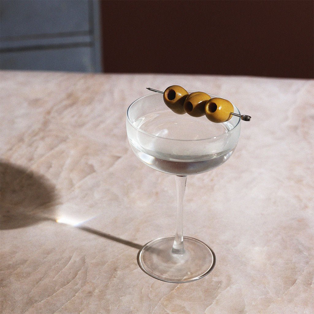 A martini cocktail in a coupe glass with an olive garnish