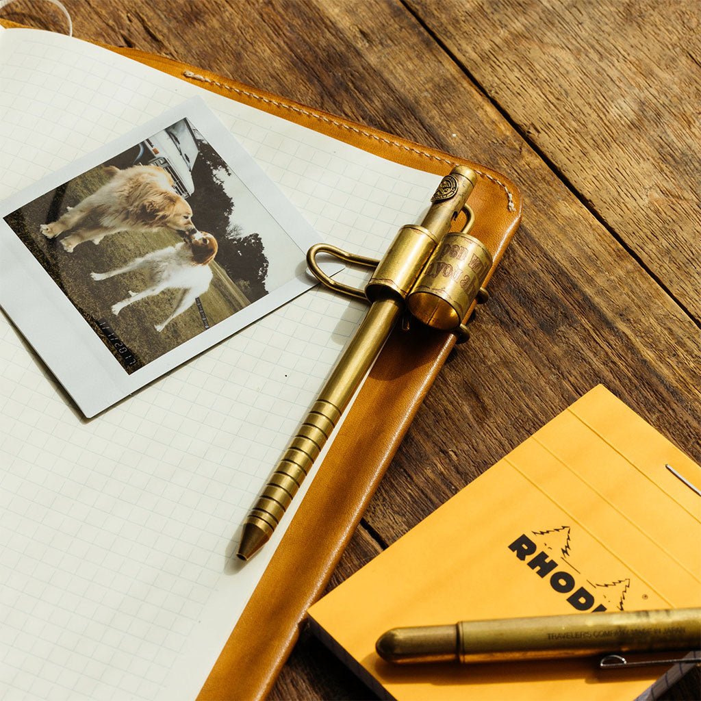 Brass pen on a wooden surface with a photo of a dog and a notebook.