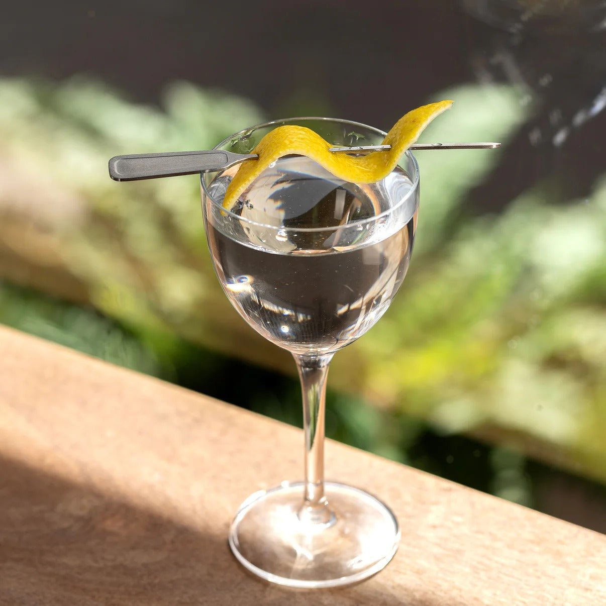 Cocktail in a glass with a lemon twist through a cocktail pick on a wooden surface