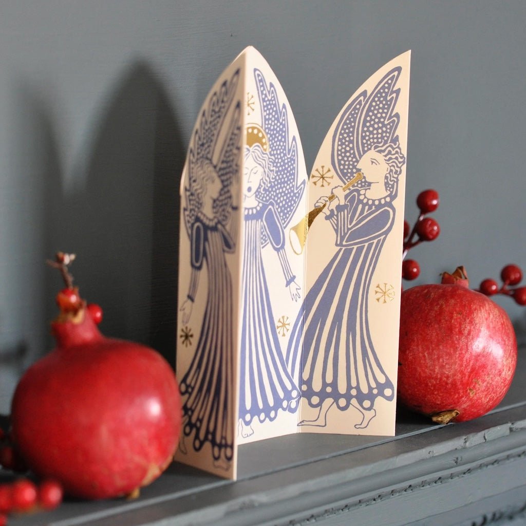 Triptych card standing on mantel next to red pomegranates.