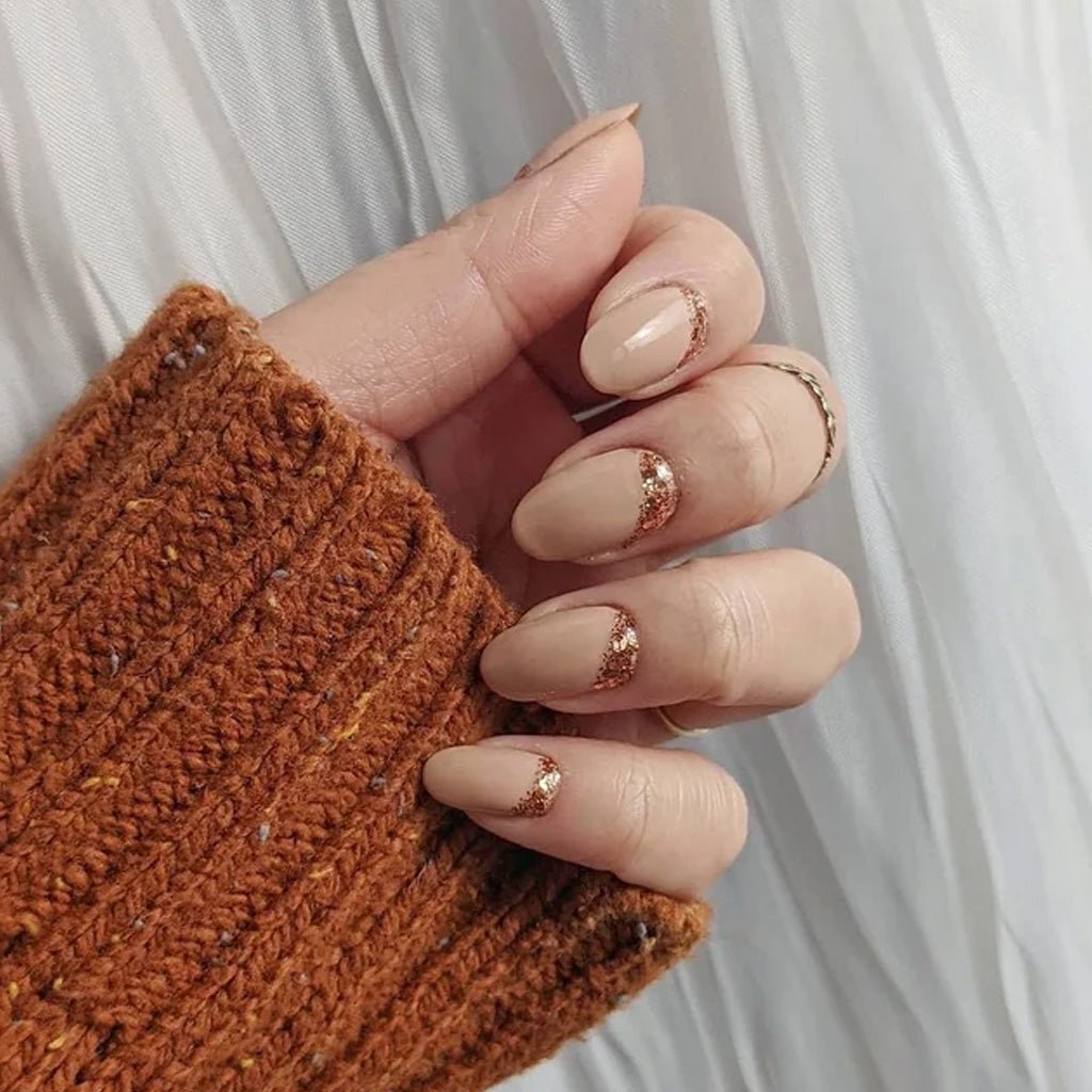 Hand wearing neutral nail polish with glittery candied ginger accents against light background