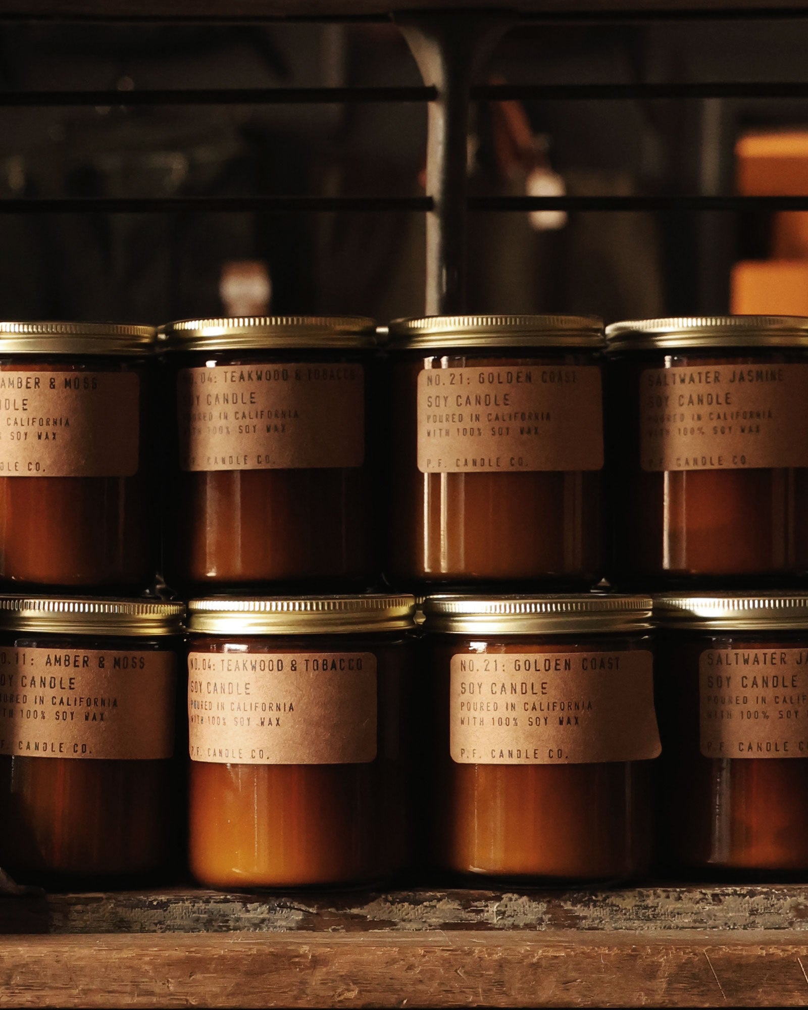 Rows of glass jar soy candles with metal lids arranged on a wooden shelf.