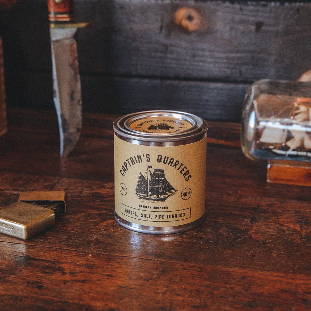 Captain's Quarters candle tin on a wooden surface with vintage items in the background