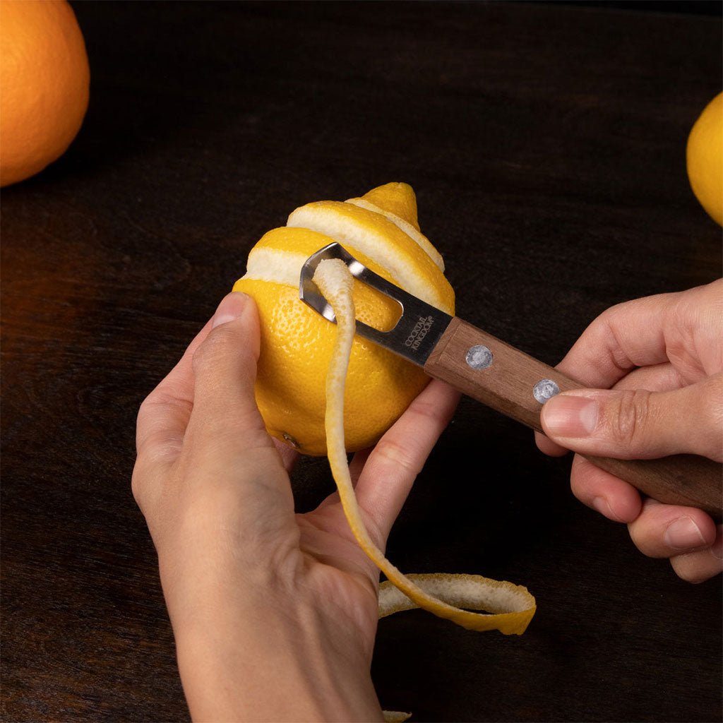 Hands peeling lemon with Wooden channel knife with rivets on wooden surface