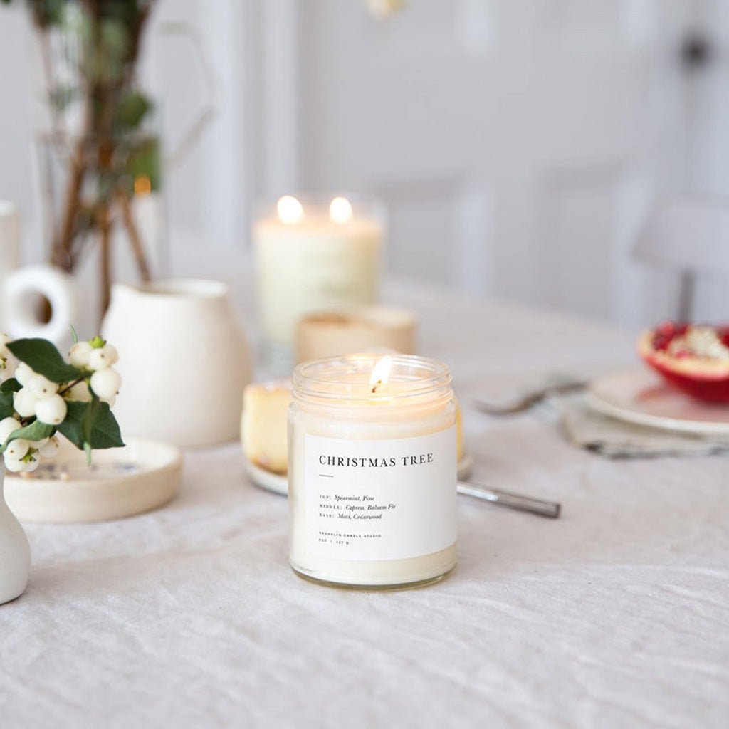 Candle labeled 'Christmas Tree' on a table with other candles and decor items.