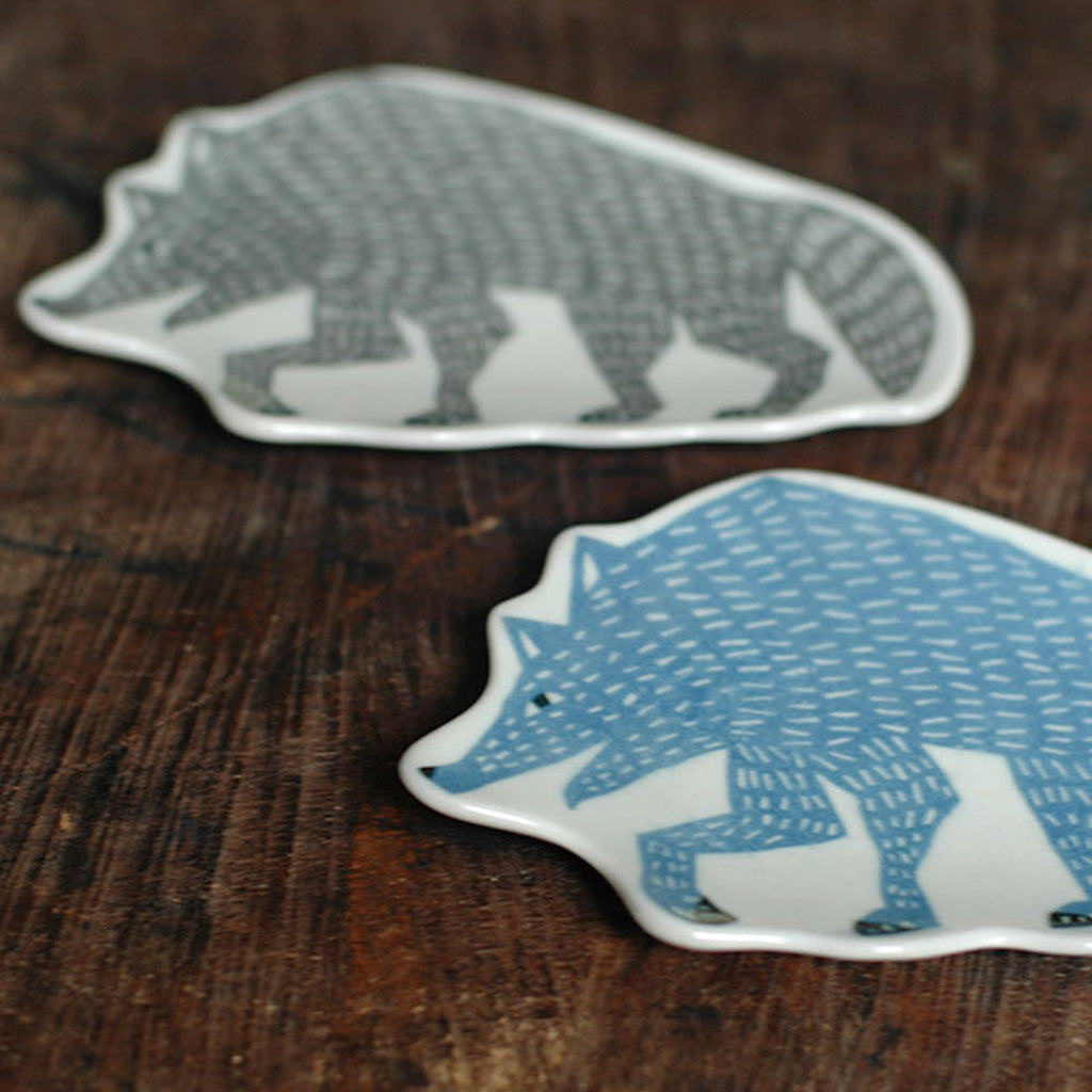 Two ceramic wolf-shaped plates with hand-painted wolf illustrations, one in gray and one in blue, displayed on a rustic dark wood surface.