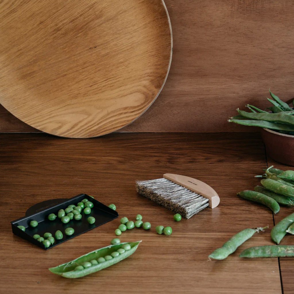 Green peas on a wooden surface with a wooden brush and metal tray.