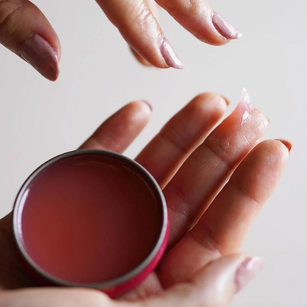 Hand holding open tin of rose salve.