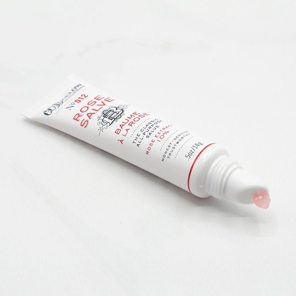 Open tube of rose salve with droplet on tip of applicator.