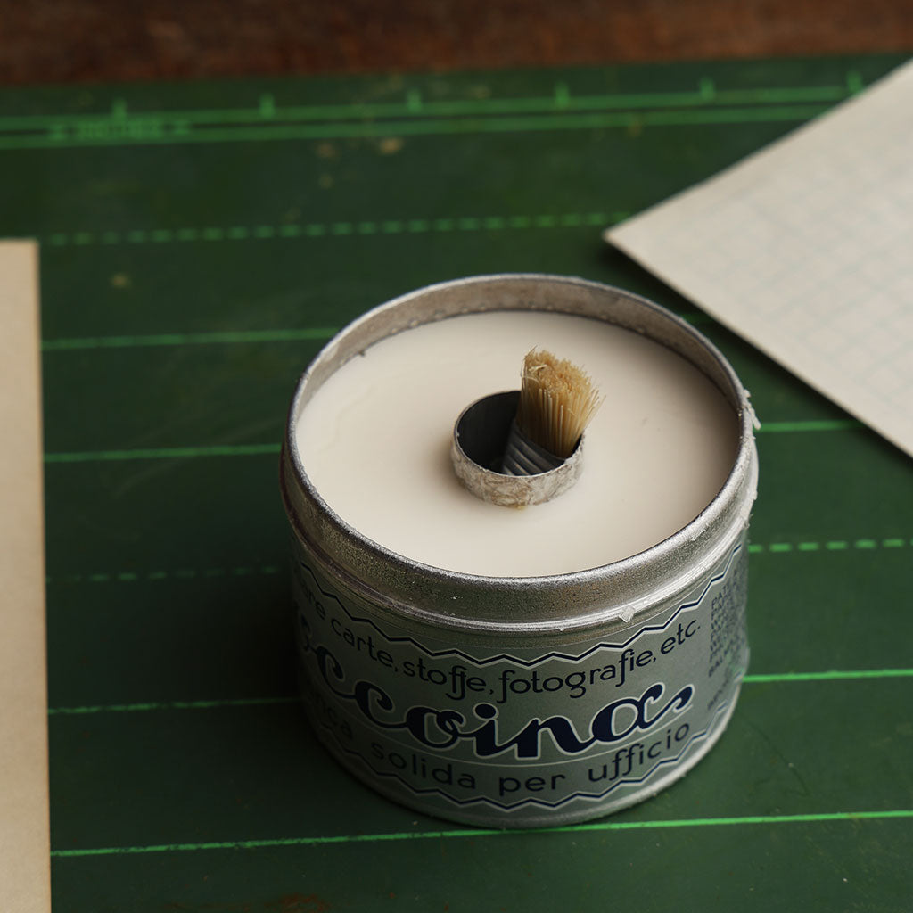 Open tin in of Coccoina adhesive paste on a green chalkboard