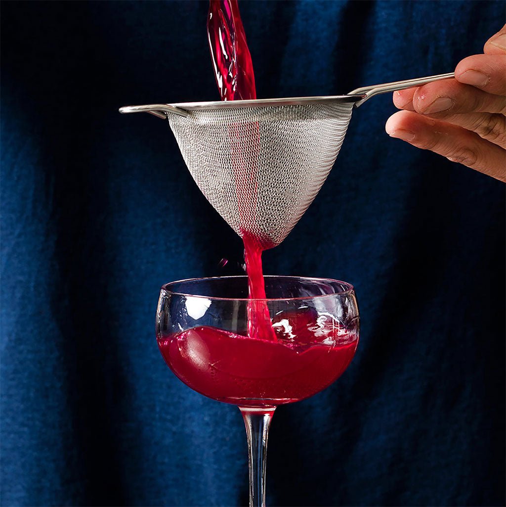 Red liquid being poured through a strainer into a glass against a dark background