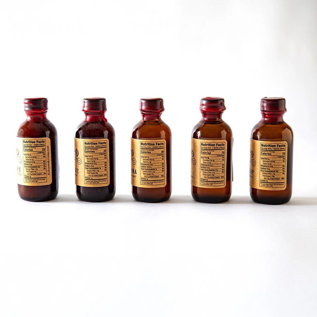 Five small brown bottles with red caps of El Guapo mixers on a white background