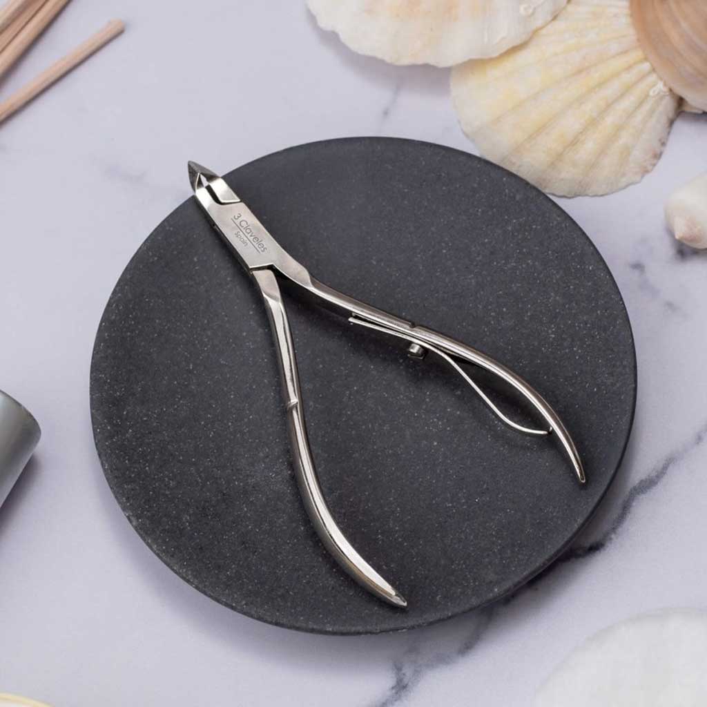 Cuticle nippers on a black stone surface with seashells in the background